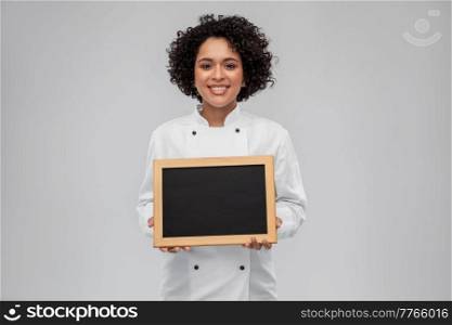 cooking, advertisement and people concept - happy smiling female chef in white jacket holding black chalkboard over grey background. smiling female chef holding black chalkboard