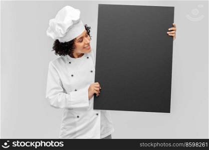 cooking, advertisement and people concept - happy smiling female chef in white jacket holding black chalkboard over grey background. smiling female chef holding black chalkboard