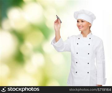 cooking, advertisement and people concept - smiling female chef, cook or baker with marker writing something on air over green background