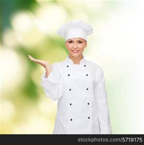 cooking, advertisement and people concept - smiling female chef, cook or baker holding something on palm of hand over green background