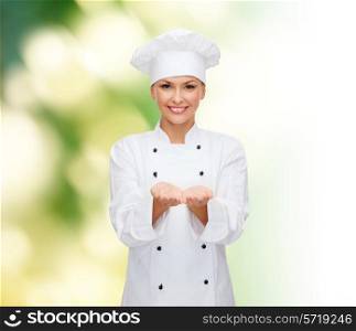 cooking, advertisement and people concept - smiling female chef, cook or baker holding something on palms of hands over green background