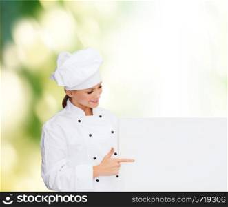 cooking, advertisement and people concept - smiling female chef, cook or baker pointing finger to white blank board over green background