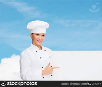 cooking, advertisement and people concept - smiling female chef, cook or baker pointing finger to white blank board over blue sky with cloud background