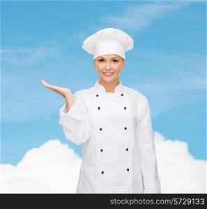 cooking, advertisement and people concept - smiling female chef, cook or baker holding something on palm of hand over blue sky with cloud background
