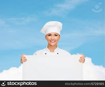 cooking, advertisement and people concept - smiling female chef, cook or baker with white blank board over blue sky with cloud background