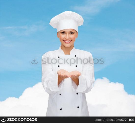 cooking, advertisement and people concept - smiling female chef, cook or baker holding something on palms of hands over blue sky with cloud background
