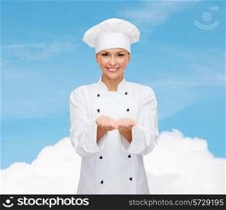 cooking, advertisement and people concept - smiling female chef, cook or baker holding something on palms of hands over blue sky with cloud background