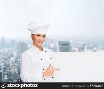 cooking, advertisement and people concept - smiling female chef, cook or baker pointing finger to white blank board over city background