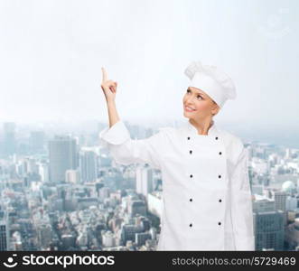 cooking, advertisement and people concept - smiling female chef, cook or baker pointing finger up to something over city background