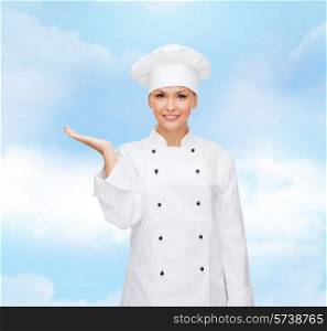 cooking, advertisement and people concept - smiling female chef, cook or baker holding something on palm of hand over blue cloudy sky background