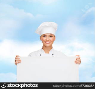 cooking, advertisement and people concept - smiling female chef, cook or baker with white blank board over blue cloudy sky background