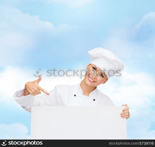 cooking, advertisement and people concept - smiling female chef, cook or baker pointing finger to white blank board over blue cloudy sky background