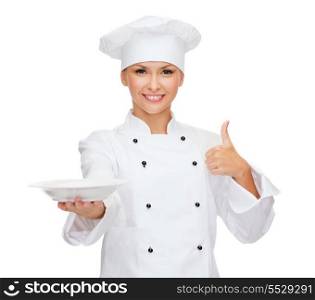 cooking and food concept - smiling female chef, cook or baker with empty plate showing thumbs up