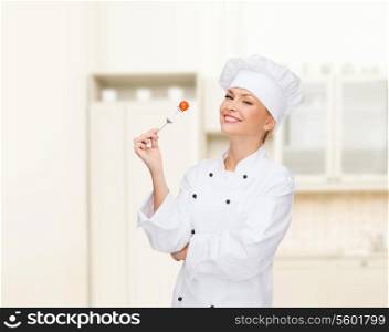 cooking and food concept - smiling female chef, cook or baker with fork and tomato