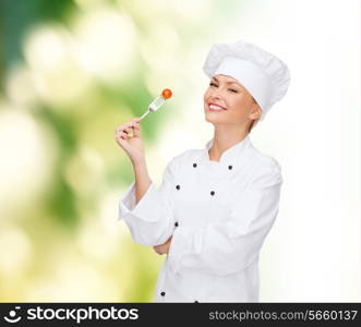 cooking and food concept - smiling female chef, cook or baker with fork and tomato