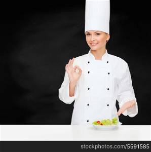 cooking and food concept - smiling female chef with salad on plate and ok sign
