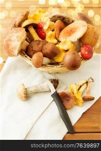 cooking and harvest concept - basket of different edible mushrooms, kitchen knife and towel on wooden table. basket of different edible mushrooms and knife
