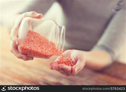cooking and home concept - close up of female emptying jar with red lentils