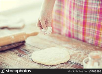 cooking and home concept - close up of female hand sprinkling dough with flour