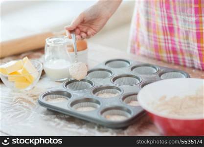 cooking and home concept - close up of hand filling muffins molds with dough