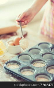 cooking and home concept - close up of hand filling muffins molds with dough