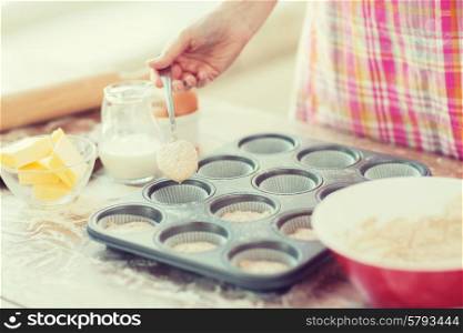 cooking and home concept - close up of hand filling muffins molds with dough