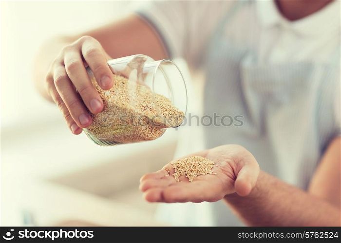 cooking and home concept - close up of male emptying jar with quinoa