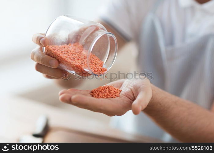 cooking and home concept - close up of male emptying jar with red lentils