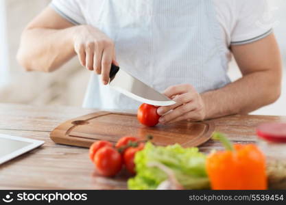 cooking and home concept - close up of male hand cutting tomato on cutting board with sharp knife