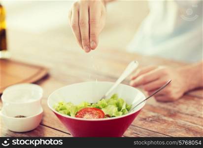 cooking and home concept - close up of male hands flavouring salad in a bowl with salt