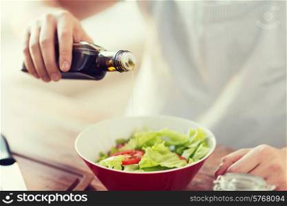 cooking and home concept - close up of male hands flavouring salad in a bowl with olive oil