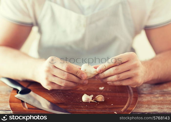 cooking and home concept - close up of male hands taking off peel of garlic on cutting board