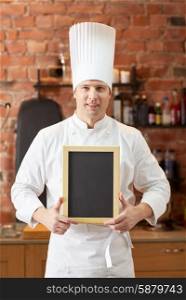 cooking and people concept - happy male chef cook with black blank menu chalk board in kitchen in restaurant kitchen