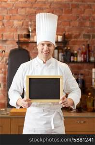 cooking and people concept - happy male chef cook with black blank menu chalk board in kitchen in restaurant kitchen