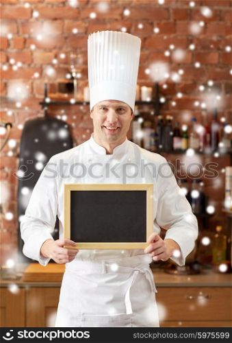 cooking and people concept - happy male chef cook with black blank menu chalk board in kitchen in restaurant kitchen over snow effect. happy male chef with blank menu board in kitchen