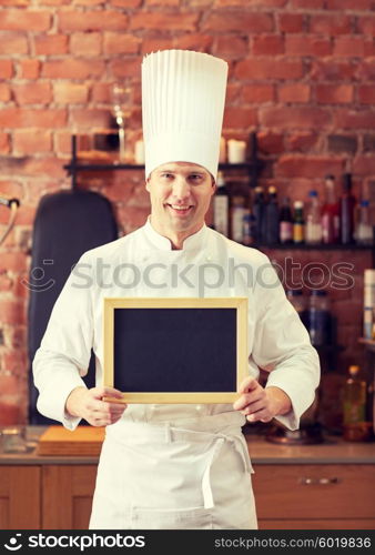 cooking and people concept - happy male chef cook with black blank menu chalk board in kitchen in restaurant kitchen. happy male chef with blank menu board in kitchen