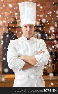 cooking and people concept - happy male chef cook with crossed hands in restaurant kitchen over snow effect. happy male chef cook in restaurant kitchen
