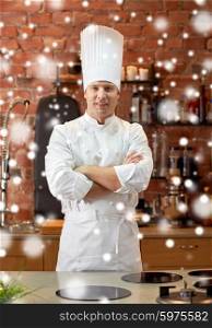 cooking and people concept - happy male chef cook with crossed hands in restaurant kitchen over snow effect. happy male chef cook in restaurant kitchen
