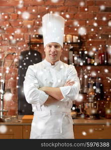 cooking and people concept - happy male chef cook with crossed hands in restaurant kitchen over snow effect. happy male chef cook in restaurant kitchen