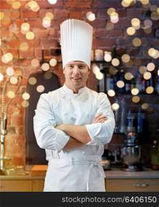 cooking and people concept - happy male chef cook with crossed hands in restaurant kitchen. happy male chef cook in restaurant kitchen