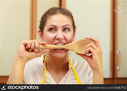 Cooking and preparing food meal concept. Thoughtful wondering and confused woman chef cook housewife holding biting ladle spoon in kitchen.. Housewife with ladle in kitchen