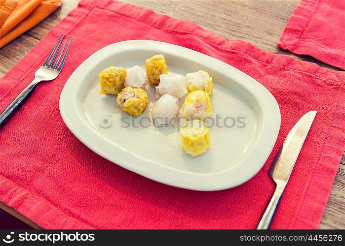 cooking, asian kitchen and food concept - plate of spring rolls with rice, fork and knife on wooden table at restaurant