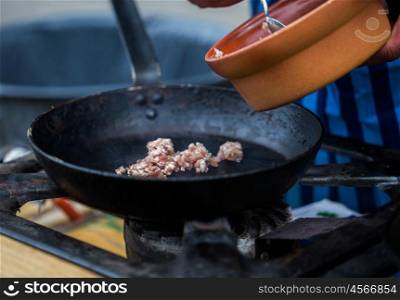 cooking, asian kitchen, sale and food concept - cook putting forcemeat on frying pan at street market on gas stove at asian street market