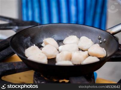 cooking, asian kitchen, sale and sea food concept - close up of scallops frying in cast iron pan at street market
