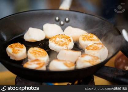 cooking, asian kitchen, sale and sea food concept - close up of scallops frying in cast iron pan at asian street market