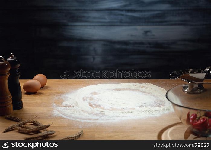 Cooking background, flour on wooden table. Low key shot, light on flour, some ingredients around on the table. Copy space.