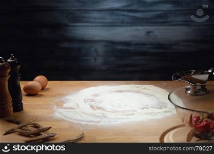 Cooking background, flour on wooden table. Low key shot, light on flour, some ingredients around on the table. Copy space.