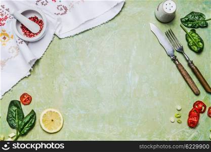 Cooking background with rustic cutlery, herbs, spices, mortar and pestle on green shabby chic wooden background, top view, frame