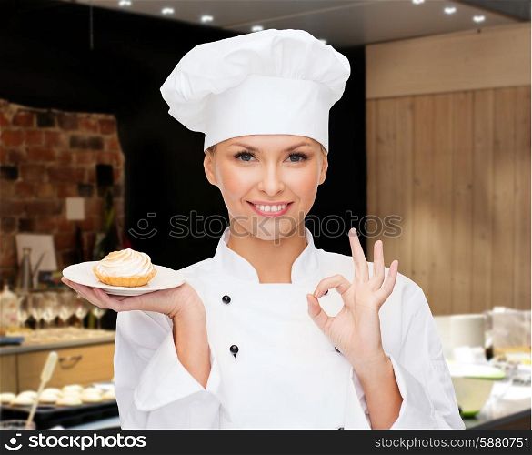 cooking, bakery, people and food concept - smiling female chef, cook or baker with cupcake on plate and ok sign over restaurant kitchen background