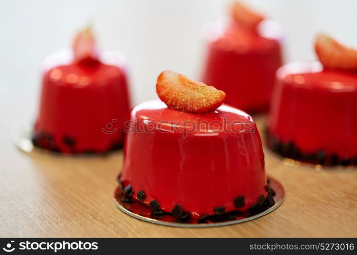 cooking, baking and food concept - strawberry mirror glaze cakes with edible gold at confectionery. strawberry mirror glaze cakes at confectionery